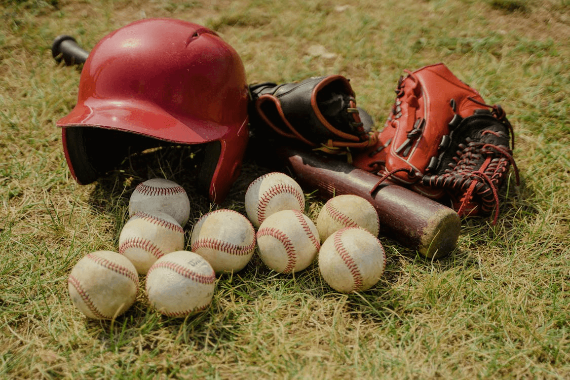 a batter's helmet, gloves, bat, and a group of baseball sitting in the grass